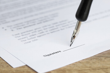 Signing notary document with fountain pen at wooden table, selective focus