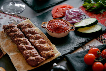 An Exquisite Platter of Grilled Kebabs Accompanied by Fresh Vegetables, Spicy Sauce, and Flatbread for a Flavorful Culinary Experience