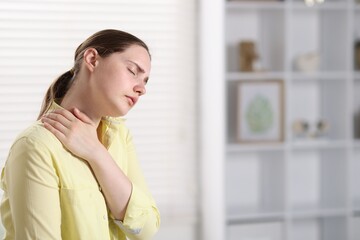 Young woman suffering from neck pain at home, space for text
