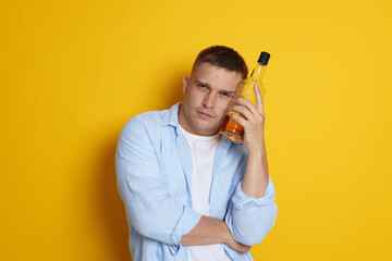 Man with bottle of whiskey suffering from hangover on orange background