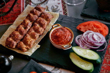 A Delicious Platter of Grilled Meat Skewers Accompanied by Fresh Vegetables and Savory Sauce, Perfect for Sharing and Enjoying a Flavorful Meal.
