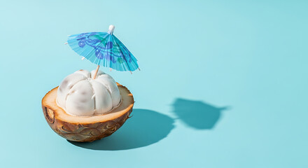 Exotic mangosteen fruit half, decorated with a paper cocktail umbrella against a serene light blue