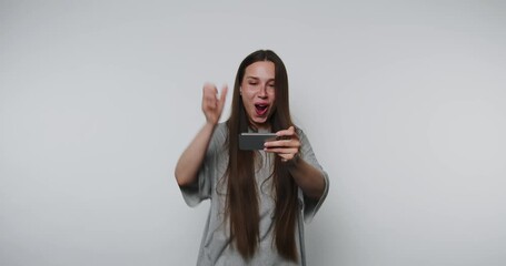 joyful young woman raises her arms in triumph while holding her smartphone, celebrating significant achievement on white background