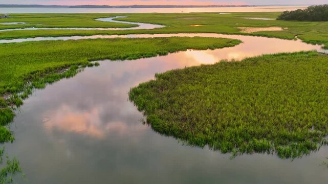 Drone Scenic sunset view over winding river surrounded by lush green marshland and tranquil waters at dusk 4k