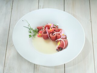 Carefully arranged slivers of fresh tuna mingle with vibrant flower blossoms and translucent onion, resting in a shallow pool of light sauce. A culinary poem unfolds before the diner