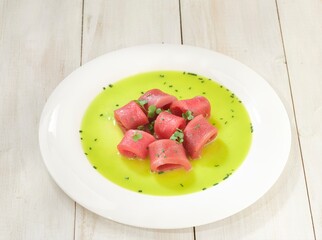 Delicate rolls of raw tuna, nestled in a vibrant green lime sauce, sit elegantly on a white plate....