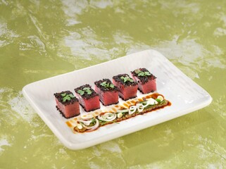 A row of five seared tuna steaks, topped with black sesame and microgreens, rest beside a complex...