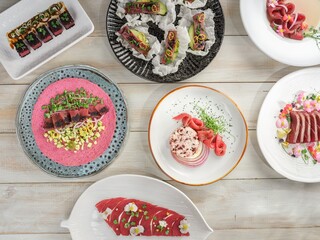 Several plates display seared tuna masterpieces. Each creation uses edible flowers, microgreens, and vibrant sauces. An elegant, artistic arrangement on a whitewashed wood table © Damian