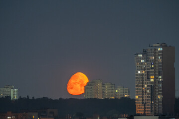 Bright orange moon sets over Kyiv skyline at night. The glowing lunar disk descends between...