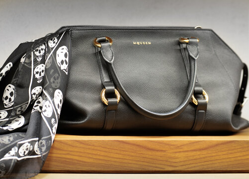 Black leather Alexander McQueen handbag with golden logo paired with silk scarf featuring skulls. Milan, Italy, 2 August 2025