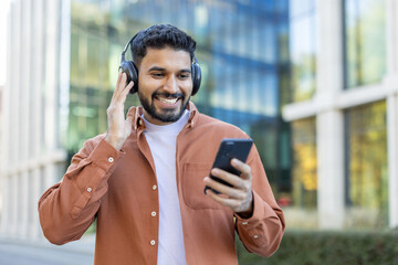 Fototapeta na wymiar A smiling man wearing headphones and looking at his smartphone in an urban setting.
