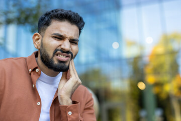 An Indian man is experiencing a painful toothache, expressing discomfort by touching his cheek.