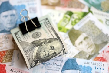 Roll of US dollar bills lies on big amount of Pakistan rupees banknotes close up