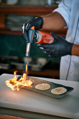 Culinary Mastery: A Chef Skillfully Uses a Torch to Ignite Flames on Delicate Tortillas, Showcasing Precision and Technique in Modern Cooking.