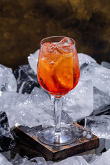 Aperol Spritz cocktail with orange slices and ice cubes in a wine glass, served on a wooden block with crushed ice. Refreshing summer drink, perfect for bars, menus, and lifestyle use.