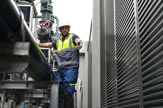 Worker inspecting industrial piping in a modern facility during daylight hours