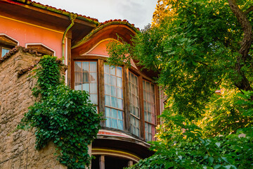 Traditional Bulgarian Revival house facade with wooden bay windows and ivy-covered stone wall charm...