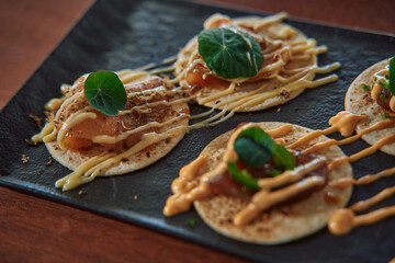 Delicious Gourmet Tacos Featuring Fresh Fish, Creamy Sauces, and Vibrant Green Garnish on a Stylish Black Plate