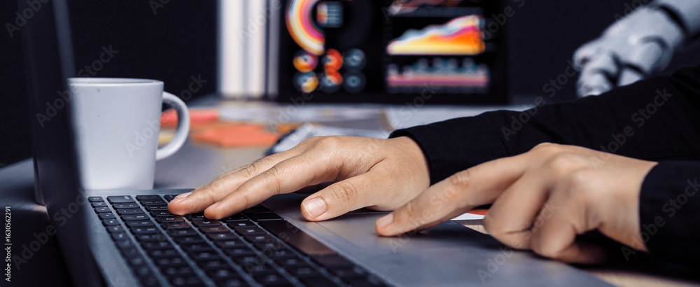 Poster a close-up view of a person typing on a laptop in a modern workspace, with colorful data visualizati
