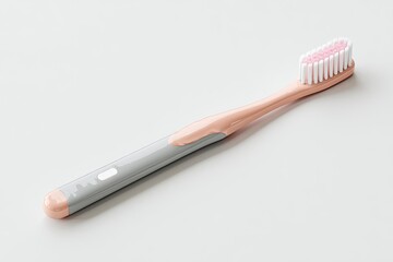 A light peach and gray toothbrush lies diagonally on a white surface.  The brush head is light pink, and the handle is a combination of peach and gray.  The handle has a slightly textured surface