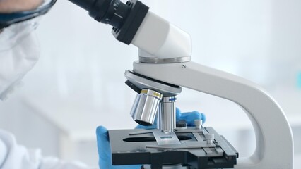 Close up of microscope and scientist's hands in blue gloves adjusting it in laboratory. Medicine,...
