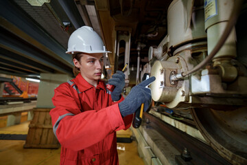 Young technician repairs machinery under industrial structure during daytime