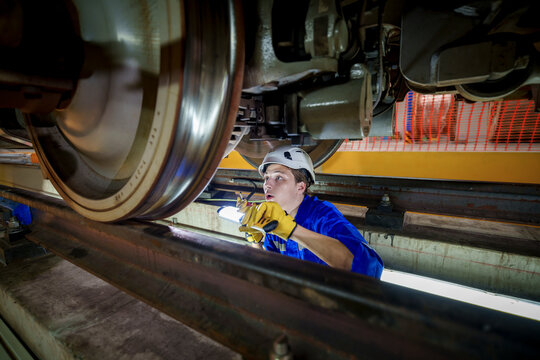 Technician inspecting train wheels in a maintenance facility at night