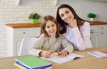 Help for son with homework from mother, happy mom and boy sitting at kitchen table to study. Young woman teaching child, student holding pencil to write in notebook. Parenthood, school concept