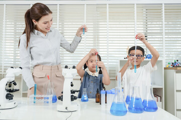 Caucasian female teacher with two asian students in classroom conducting science experiment using...