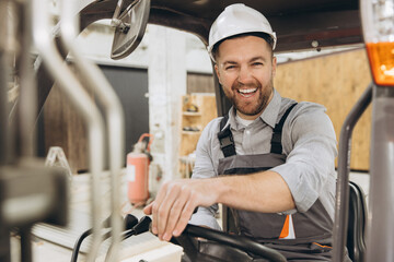 Smiling construction worker driving forklift in modular building factory