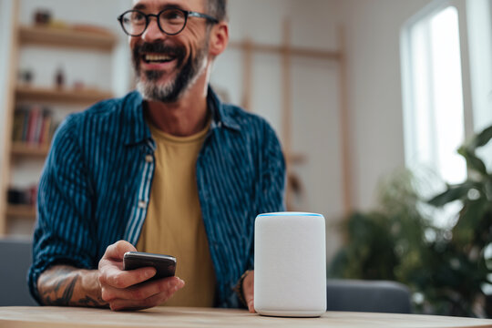 A man is sitting at a table with a white speaker and a cell phone - Powered by Adobe
