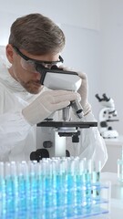 Male virologist in medical gown and gloves examines virus samples under microscope while conducting...