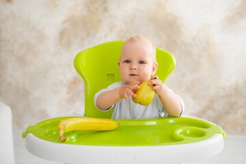 feeding a baby boy with fruit puree in a green high chair, baby food