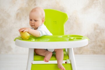 feeding a baby boy with fruit puree in a green high chair, baby food