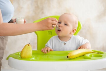 feeding a baby, mother feeding a baby boy with a spoonful of fruit puree in a green high chair, baby food