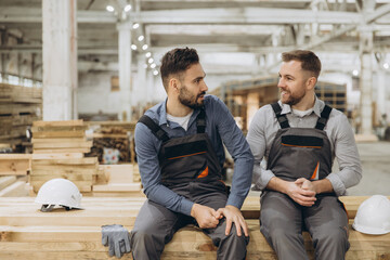 Two carpenters discussing while sitting on wood planks in workshop