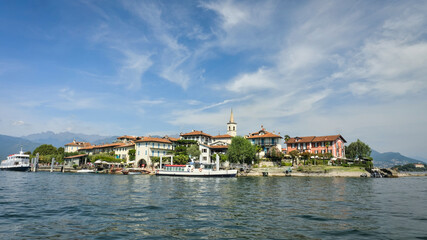 Isola Superiore (Isola dei Pescatori), Italy: A scenic view of the picturesque island on Lake Maggiore, with historic buildings, a prominent bell tower, and ferries docked at the shore.