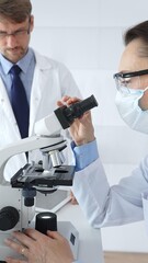 Two scientists, a man and a woman, in lab coats and protective gear, conduct research in a sterile...