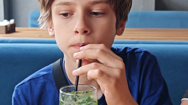 Close-up of a teenage boy drinking a sugary soda. Young Caucasian guy is sitting in a fast food restaurant - and drinking a cold drink using a plastic tube