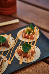 Delicious Small Tacos Topped with Fresh Fish, Creamy Sauce, and Garnishes Served on a Rustic Wooden Table