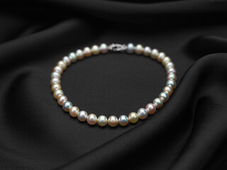 Fototapeta premium Multi colored pearl necklace on black silk fabric pearls