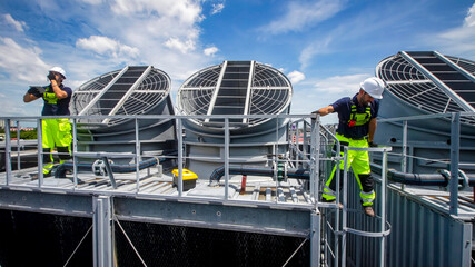 Workers performing maintenance on rooftop cooling units in a bright sky