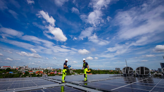 Workers install solar panels on a rooftop under a bright blue sky in an urban setting