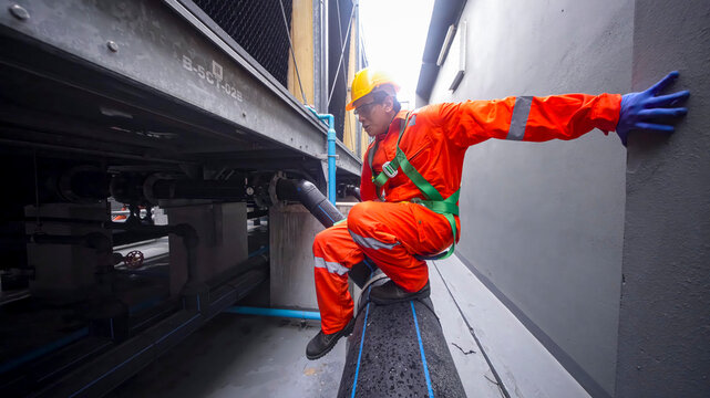 Worker in safety gear navigates tight space in industrial setting during daylight hours