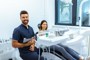 Obraz premium Male Dentist Posing with Tablet and Female Patient in Background