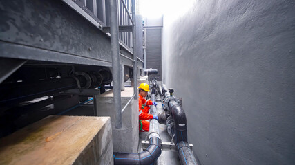 Worker repairing pipes in narrow industrial space during daylight hours