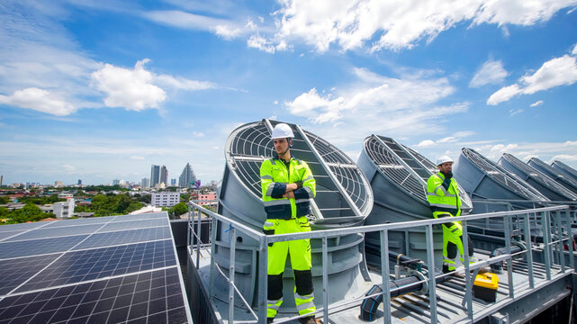 Workers perform maintenance on rooftop cooling systems in a sunny urban setting