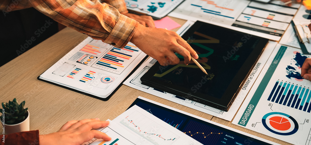 Poster a business team collaborates over various financial reports, charts, and graphs on a workspace table
