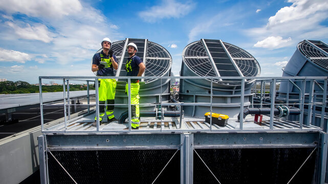 Workers conduct maintenance on rooftop cooling systems under a clear blue sky
