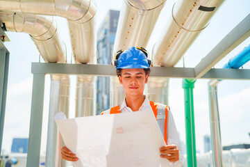 Young engineer examines blueprints at construction site during sunny afternoon